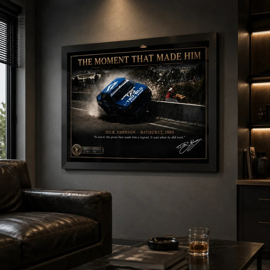 Black framed Dick Johnson Bathurst 1980 motorsport wall art displayed in a dark man cave beside leather seating.