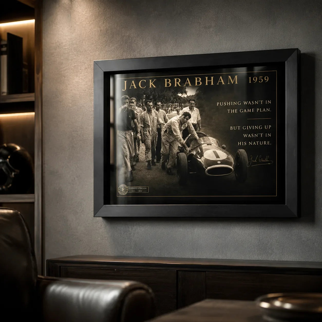 Black-framed Jack Brabham motorsport wall art on a dark textured wall in a premium man cave with leather seating.