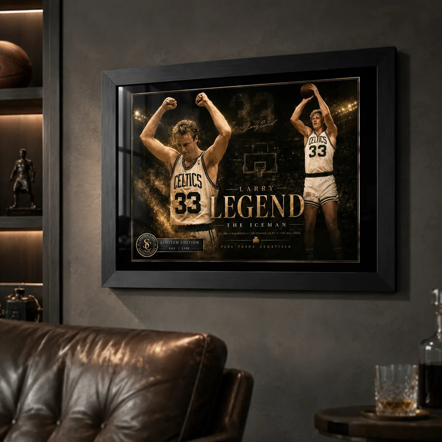 Larry Bird wall art in black frame displayed on a dark man cave wall beside leather seating and sports shelves.