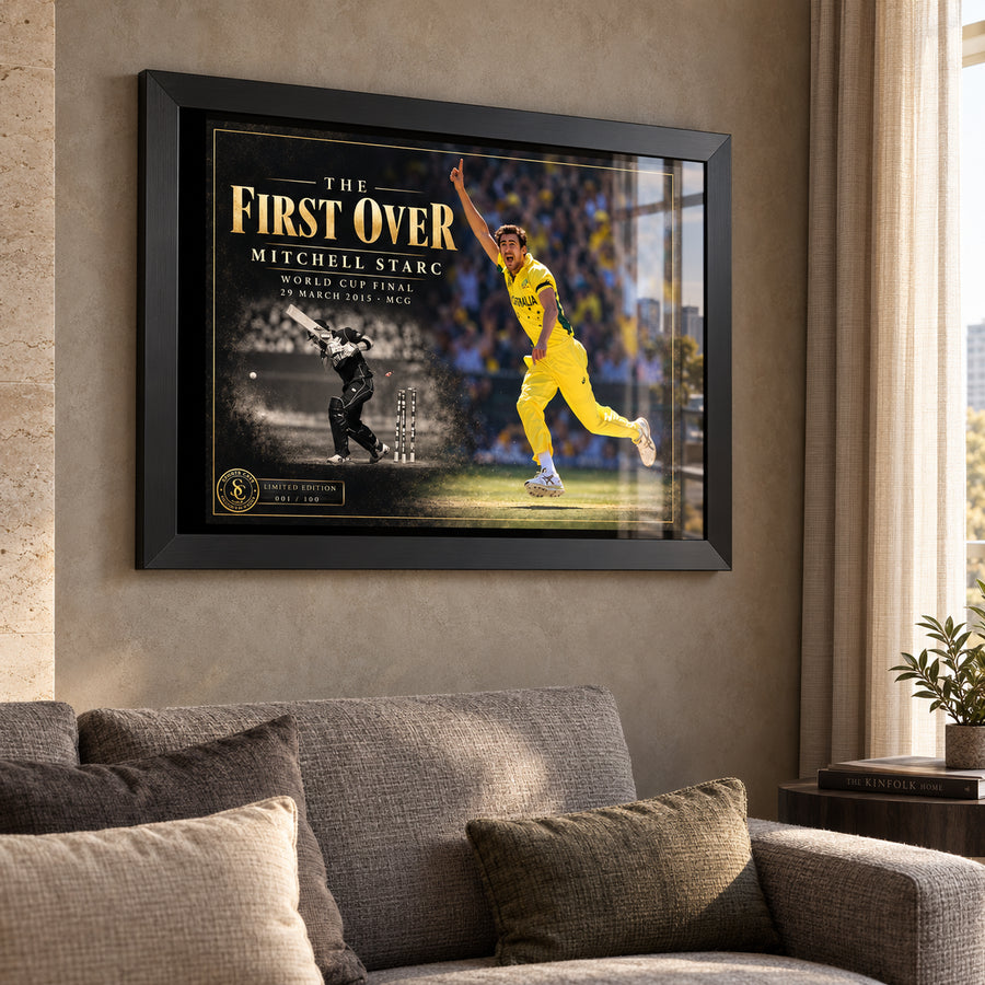 Mitchell Starc The First Over edition in a black frame above a grey sofa beside a sunlit living-room window.