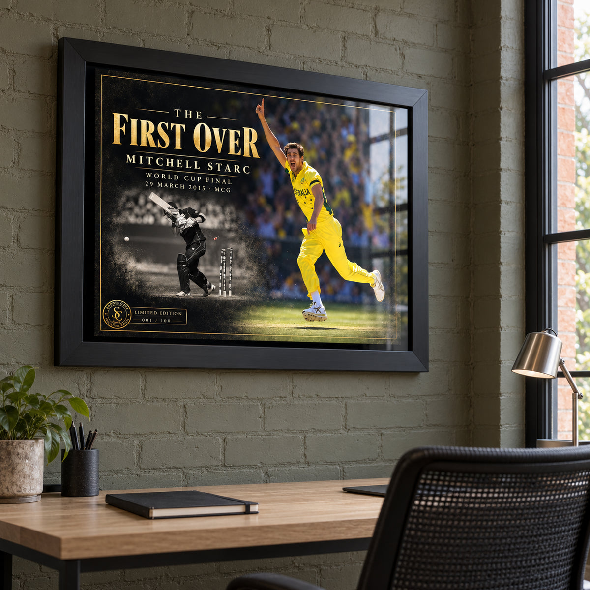 Mitchell Starc The First Over edition in a black frame above a timber desk against a pale brick home-office wall.