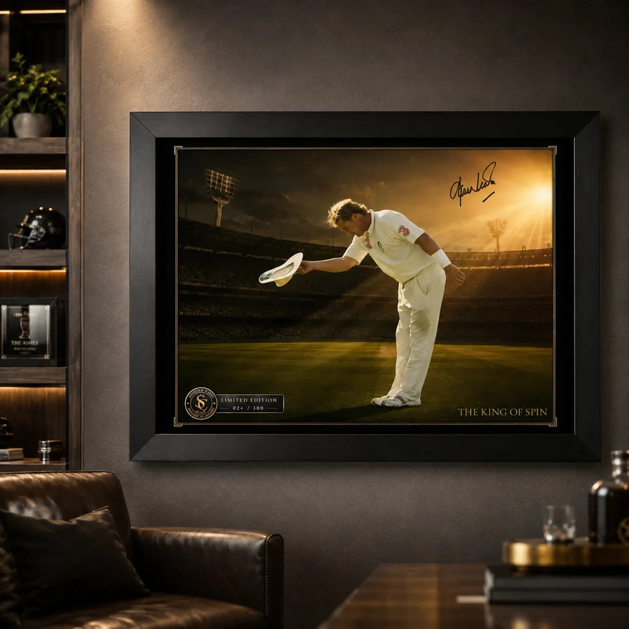 Black framed Shane Warne cricket wall art displayed on a charcoal man cave wall beside warm timber shelving.
