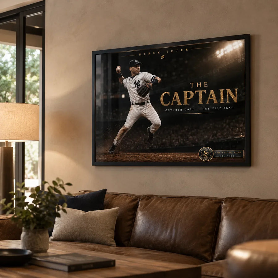 Black framed Derek Jeter The Captain baseball wall art displayed above a brown leather sofa in a warm living room.