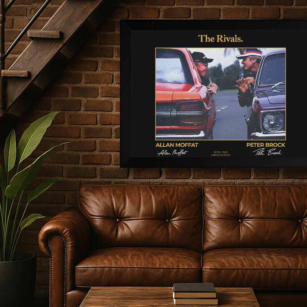 Framed “The Rivals” wall art of Peter Brock and Allan Moffat displayed in a stylish man cave with leather couch, brick wall, and warm lighting – perfect decor for motorsport fans and collectors.