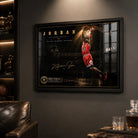 Basketball dunk wall art in a black frame on a dark man cave wall with sports memorabilia nearby.