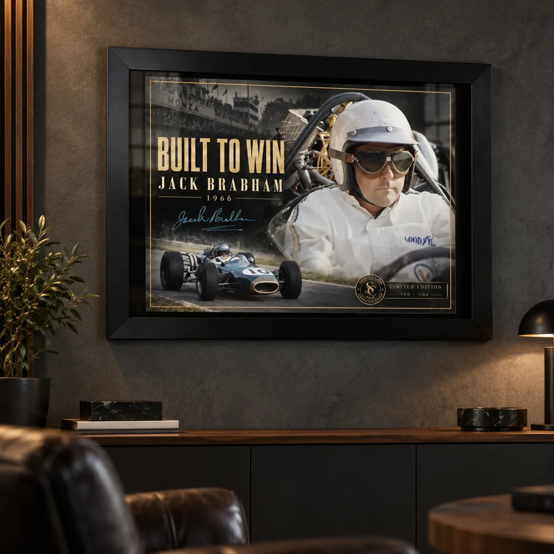 Jack Brabham Built To Win 1966 motorsport wall art in a black frame on a dark man cave wall above leather seating.