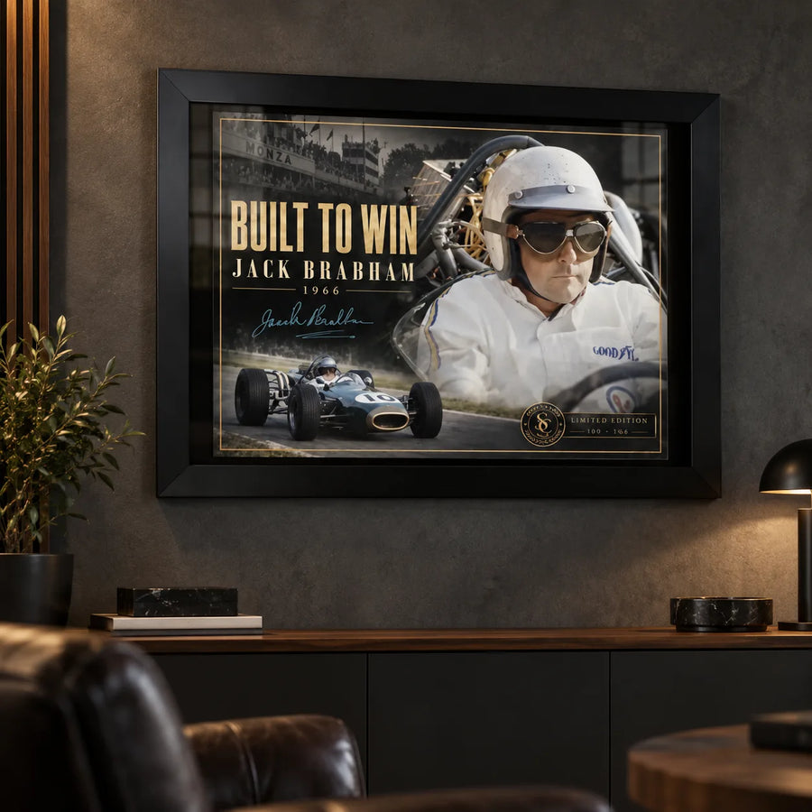 Jack Brabham Built To Win 1966 motorsport wall art in a black frame on a dark man cave wall above leather seating.