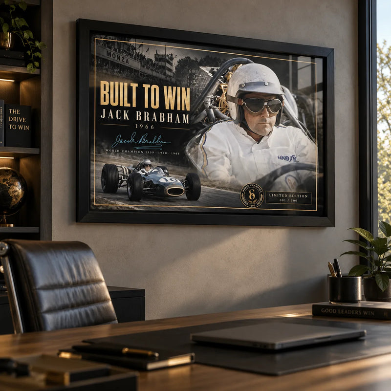 Black framed Jack Brabham Built To Win 1966 motorsport wall art displayed in a modern office above a timber desk.