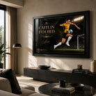 Caitlin Foord soccer wall art in a black frame displayed above a low console in a modern living room.