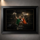 Black framed Conor McGregor wall art showing The Notorious beneath arena lights with both championship belts raised.