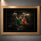 Oak framed Conor McGregor wall art featuring The Notorious beneath arena lights with both championship belts raised.