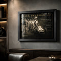 Black-framed Jack Brabham motorsport wall art on a dark textured wall in a premium man cave with leather seating.