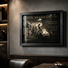 Black-framed Jack Brabham motorsport wall art on a dark textured wall in a premium man cave with leather seating.