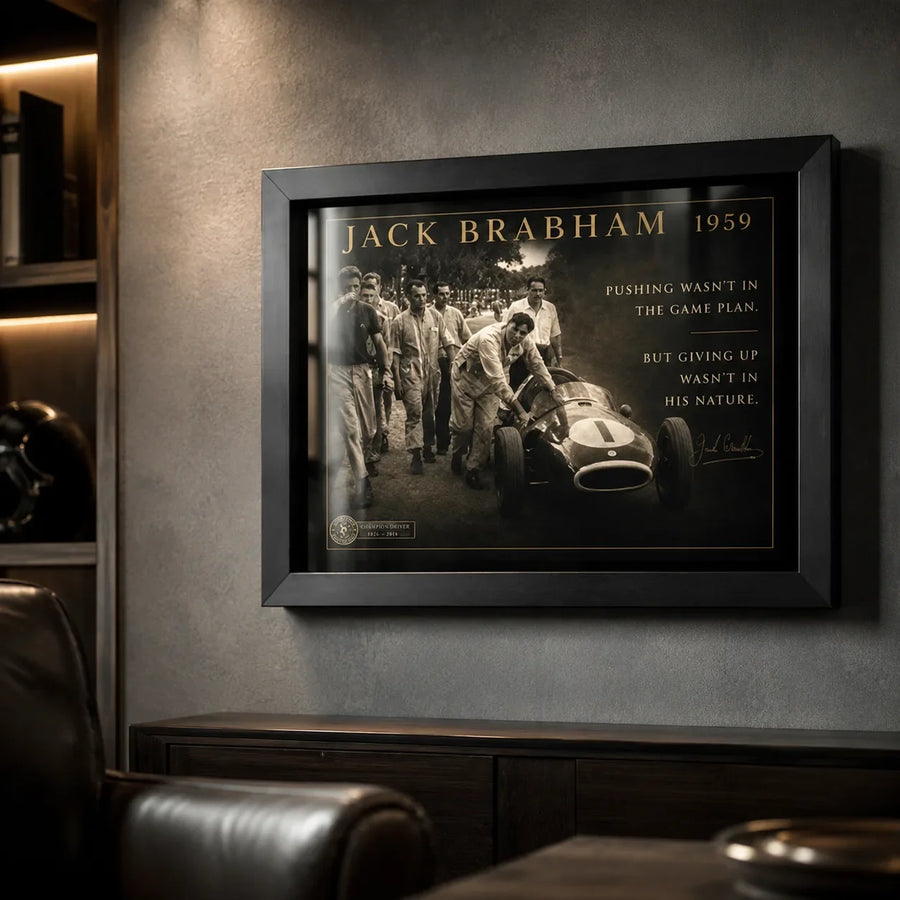 Black-framed Jack Brabham motorsport wall art on a dark textured wall in a premium man cave with leather seating.