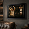 Larry Bird wall art in black frame displayed on a dark man cave wall beside leather seating and sports shelves.