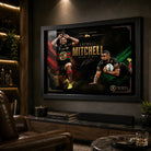 Black framed Latrell Mitchell wall art displayed in a dark man cave with warm shelving and leather seating.