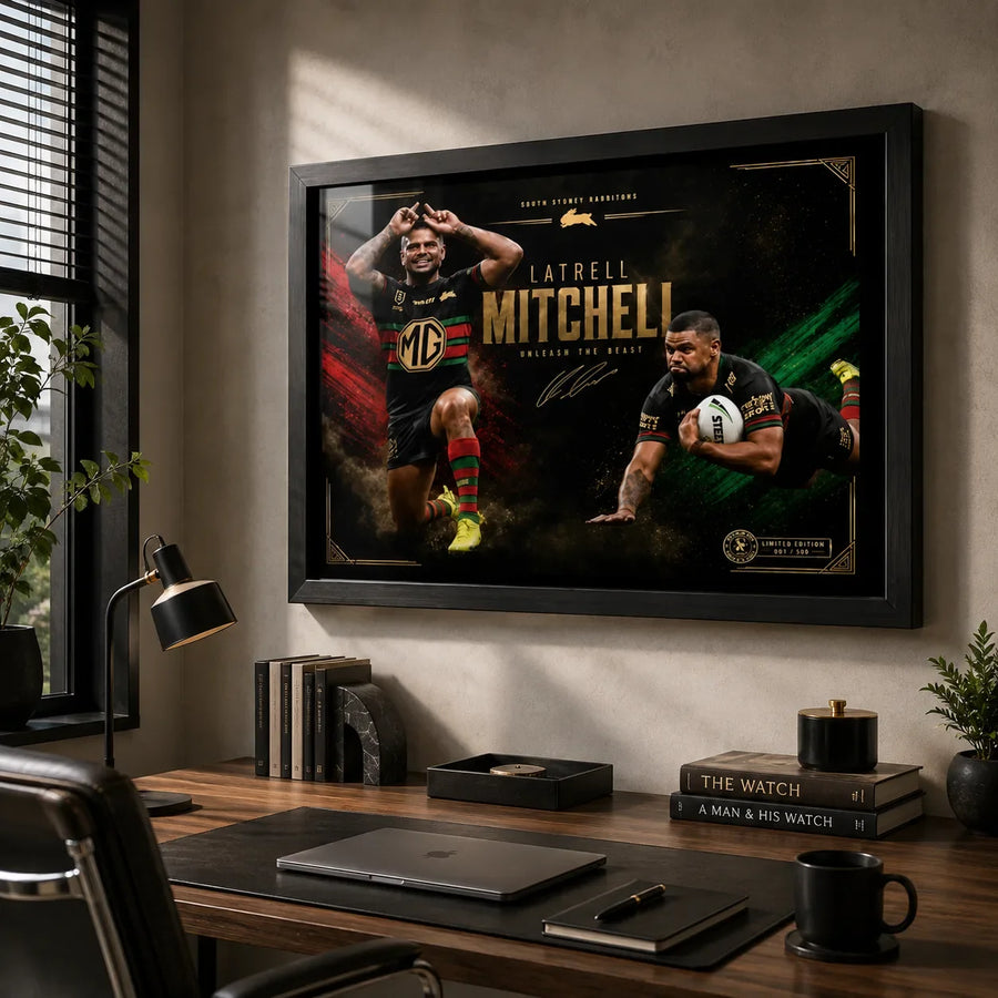 Black framed Latrell Mitchell wall art displayed above a timber desk in a modern home office with natural light.