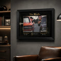 Black framed motorsport rivalry wall art styled in a dark man cave with collector display shelves