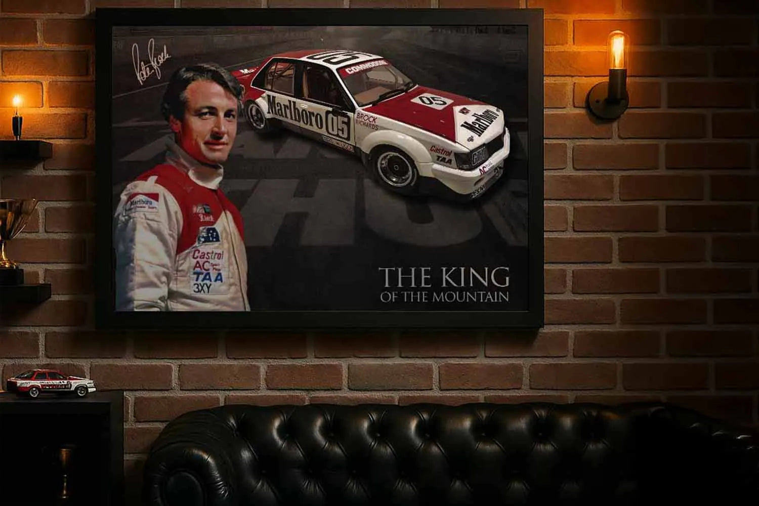 Peter Brock King of the Mountain framed print on brick man cave wall above leather sofa.