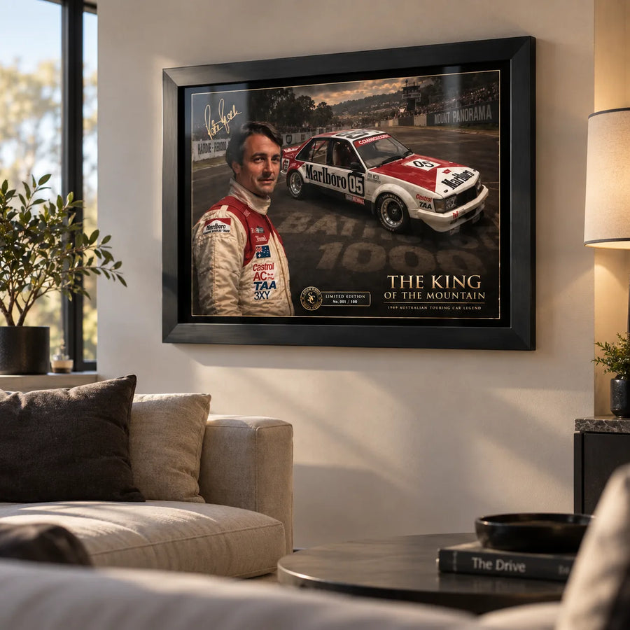 Black framed Peter Brock Tribute motorsport wall art displayed in a bright living room above a neutral sofa and coffee table.