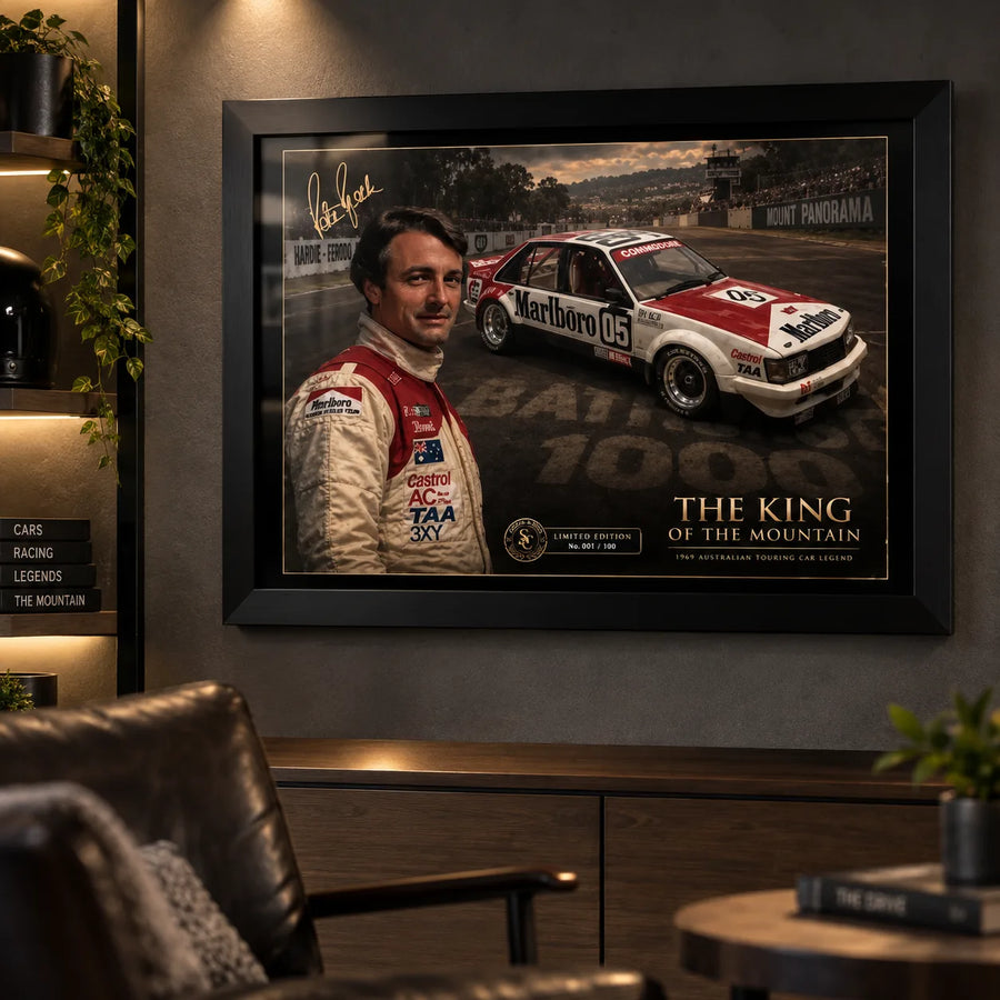 Black framed Peter Brock Tribute motorsport wall art displayed in a dark man cave with warm shelving and collector styling.