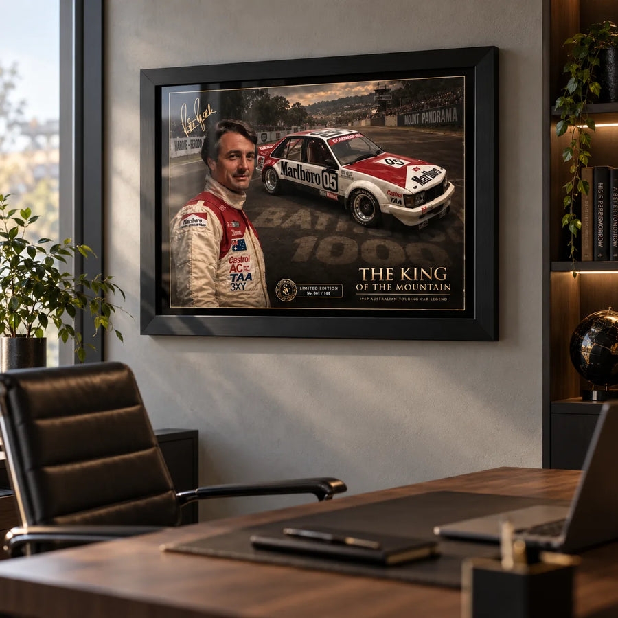 Black framed Peter Brock Tribute motorsport wall art displayed in a modern office above a timber desk and leather chair.