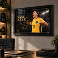 Black framed Sam Kerr Matildas soccer wall art displayed in a modern office above a desk with warm ambient lighting.