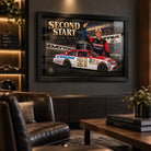 Trevor Bayne Second Start wall art displayed in a dark motorsport man cave with warm shelving and racing decor.