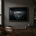Black framed Aikman and Smith wall art displayed in a dark man cave with timber cabinetry and a leather chair.