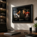Black framed Tom Brady vs Joe Montana wall art mounted in a modern office above a timber desk.