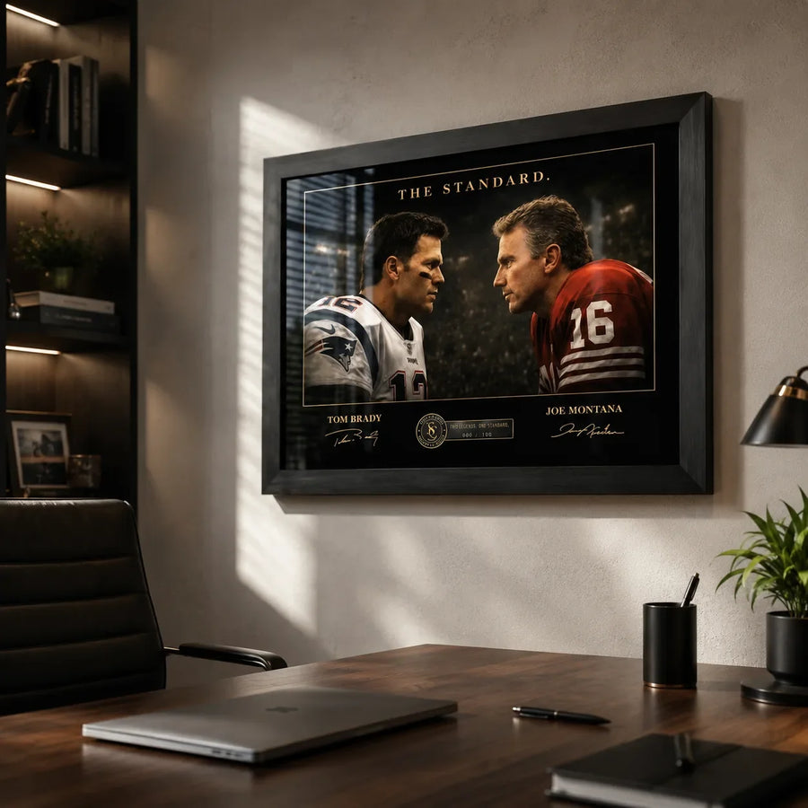 Black framed Tom Brady vs Joe Montana wall art mounted in a modern office above a timber desk.