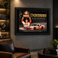 Alan Kulwicki Underbird NASCAR wall art above a brown leather chair in a dark man cave with lit collector shelves.