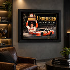 Alan Kulwicki Underbird NASCAR wall art above a brown leather chair in a dark man cave with lit collector shelves.