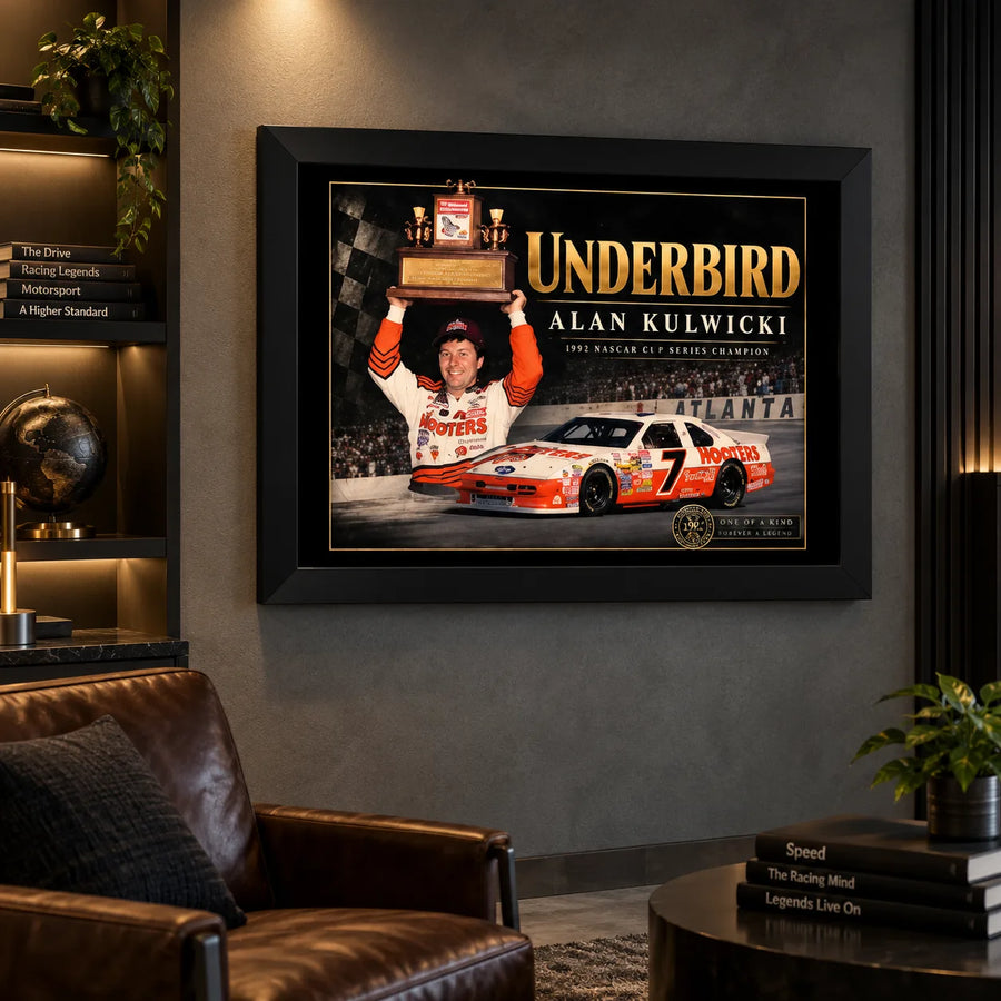 Alan Kulwicki Underbird NASCAR wall art above a brown leather chair in a dark man cave with lit collector shelves.